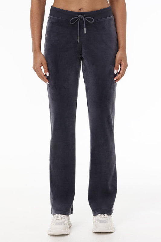 Someone wearing OG Big Bling Velour Track Pants in dark gray with a drawstring and white sneakers stands against a plain white background, shown from the shoulders down.