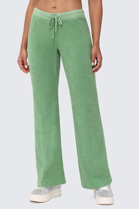 A person wears Big Bling Washed Terry Track Pants in light green with a relaxed fit and subtle rhinestone logo, paired with white sneakers. The upper body is partially visible against a plain light gray background.