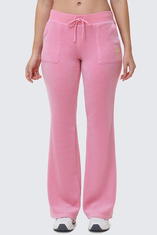A person wearing Heritage Cotton Velour Track Pants in light pink, featuring front pockets and a drawstring waist, paired with white sneakers. Shown from the midriff down against a plain background.