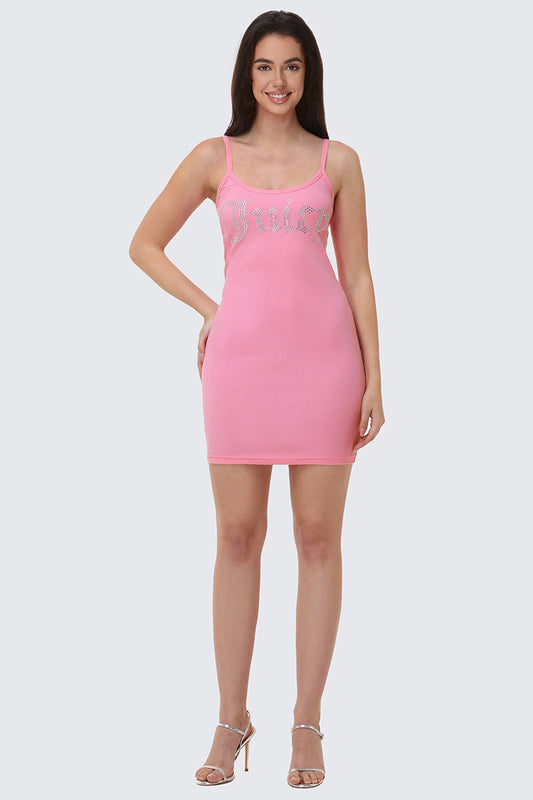 A woman smiles in the Big Bling Mini Dress—a fitted, sleeveless pink ribbed cami dress with a rhinestone Juicy logo on the chest. She has long dark hair and wears strappy high-heeled sandals, posed against a plain light grey background.