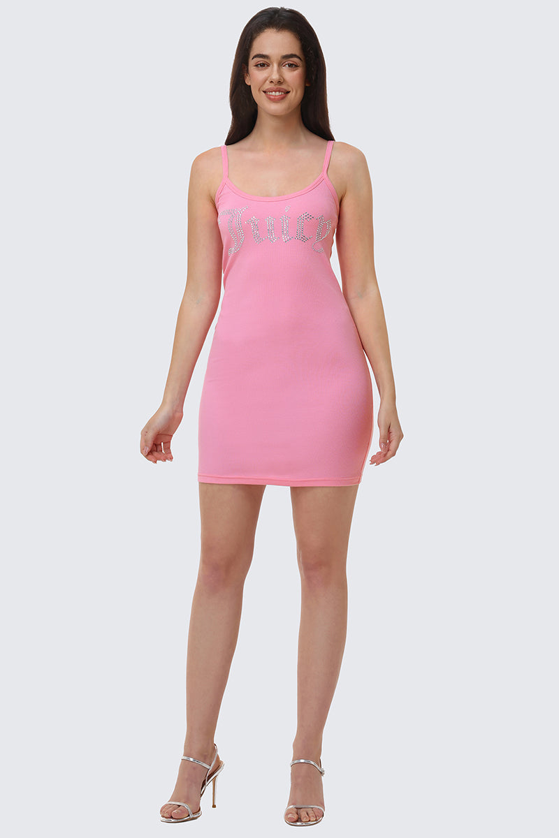 A woman wears the Big Bling Mini Dress—a pink, sleeveless, ribbed cami dress with thin straps and a rhinestone Juicy logo on the chest—paired with silver heels, standing and smiling against a plain light gray background.