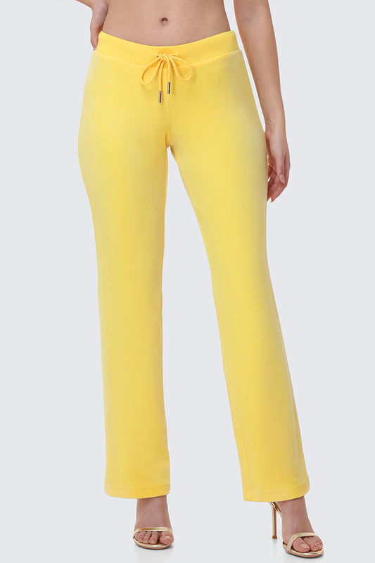 Wearing OG Big Bling Velour Track Pants in yellow and open-toe heels, a person stands against a light gray background with their upper body partially out of frame, giving off subtle Y2K vibes.