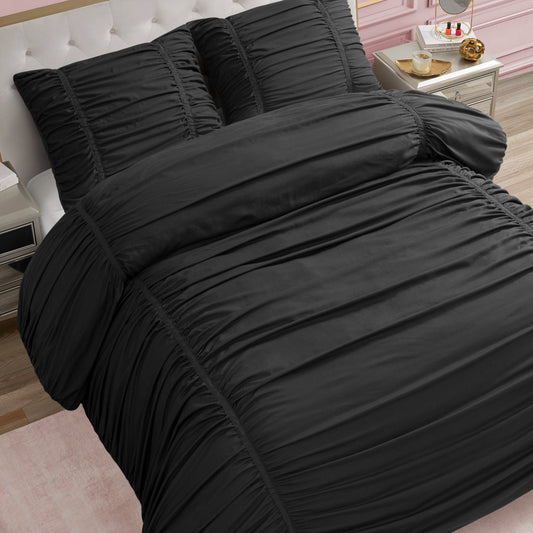 A neatly made bed features the Ribbon Ruched Comforter Set in black with matching pillows, set in a stylish bedroom with a white tufted headboard, pink wall, gold nightstand, and light wood floor.