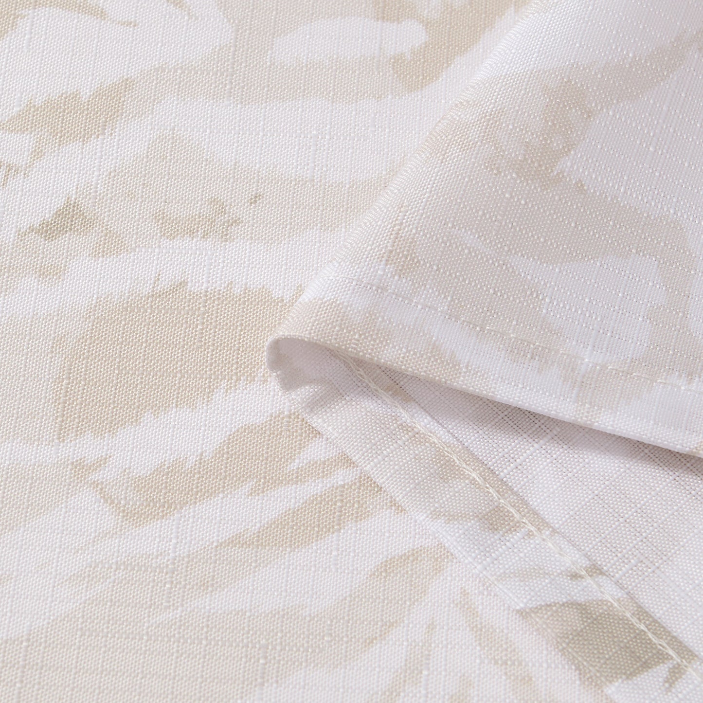 Close-up of the Stassi Shower Curtain with PEVA Liner and Hooks 14-Piece Set, featuring beige and white fabric with a subtle abstract pattern. The fabric is folded to highlight its texture and neatly stitched edges—perfect for elevating your bath decor or making a statement in your bathroom ensemble.