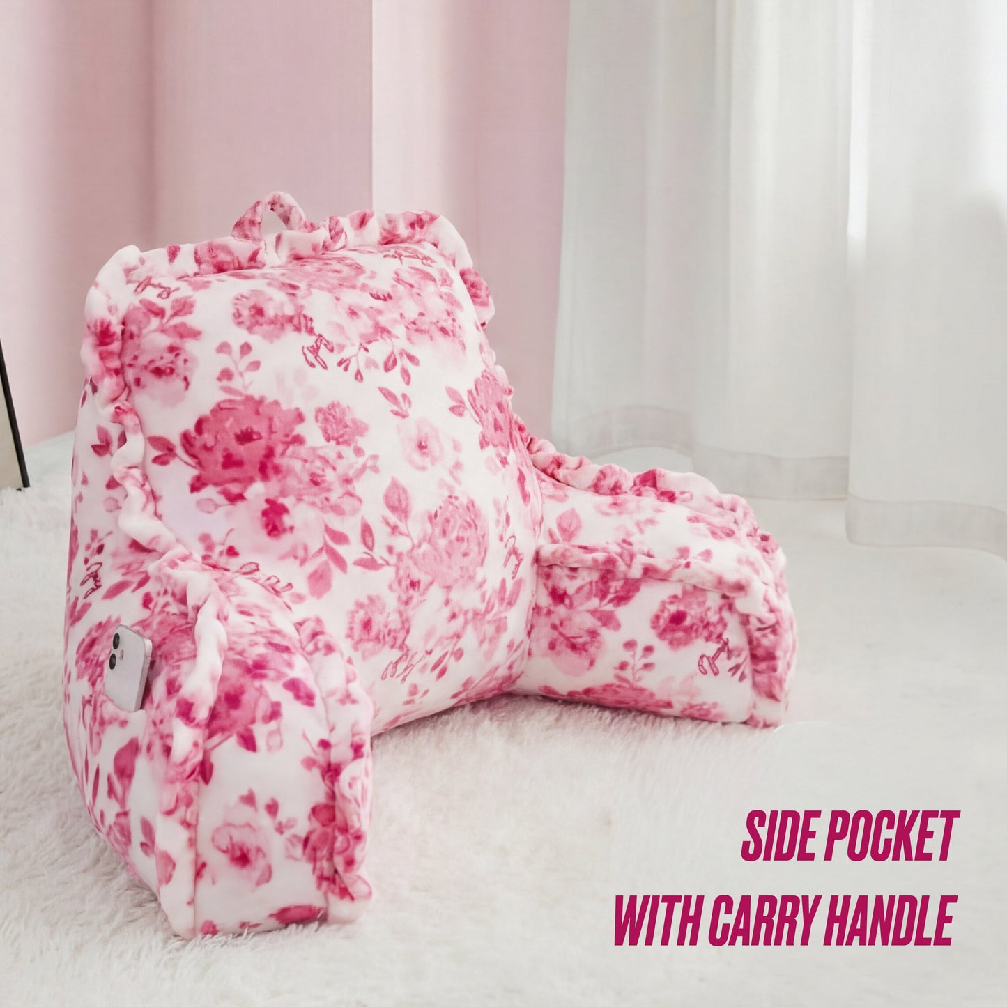 The Backrest Pillow by Juicy Couture features a pink and white floral design, side arms, a carry handle, and a convenient side pocket for your smartphone. Text reads: SIDE POCKET WITH CARRY HANDLE.