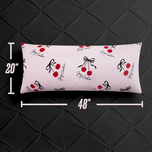 The Plush Body Pillow by Juicy Couture measures 20"x48" and features a chic light pink cover with red cherries, black bows, and "Jigy Chatrie" cursive, displayed against a black quilted background.