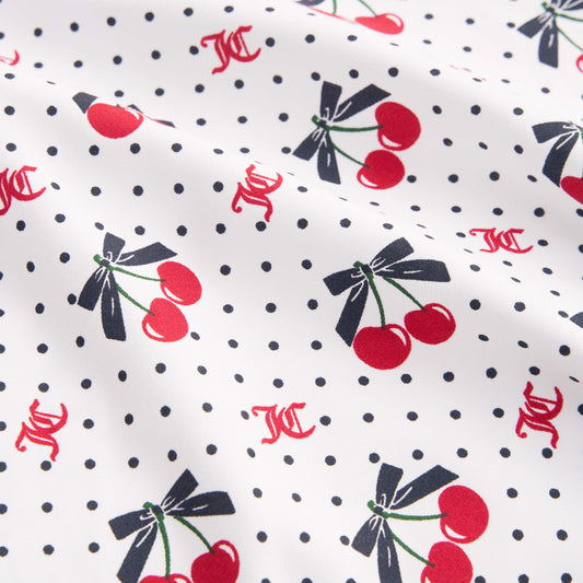 The Printed Microfiber Sheet Set features white fabric with small black polka dots, red cherries tied with black bows, and scattered red KC initials for a playful Juicy Couture touch. Slightly wrinkled for relaxed luxury bedding style.