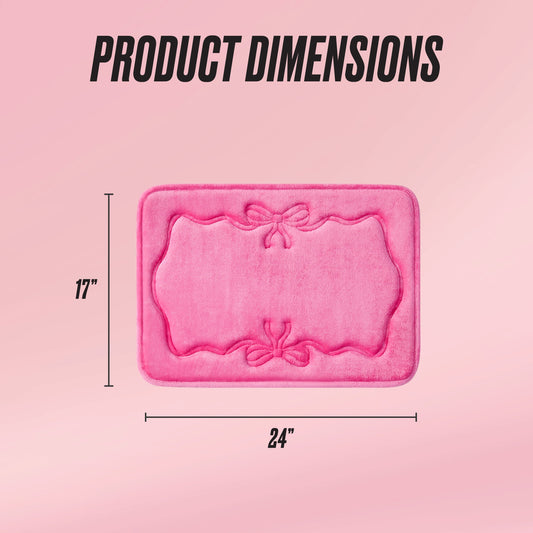 A pink Quilted Memory Foam Bath Mat, 17" x 24", with decorative bows and ornate borders, is shown on a pink gradient background with "PRODUCT DIMENSIONS" displayed above.