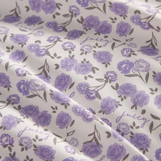 This Printed Microfiber Sheet Set features a white background with purple roses, green leaves, and "juicy" in cursive for a delicate floral look. Softly draped fabric adds a touch of luxury to any bedroom.