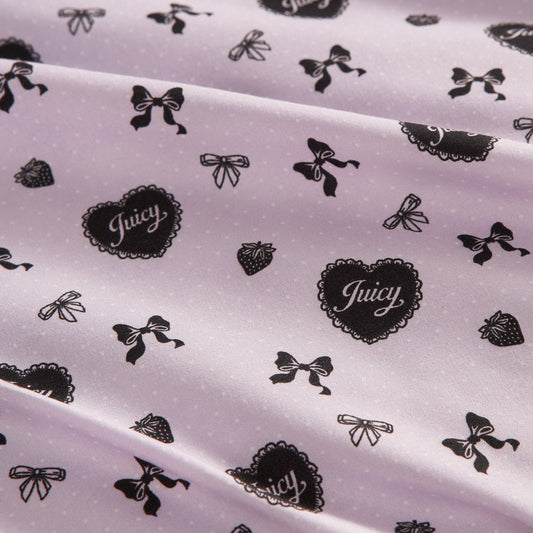 Close-up of the Printed Microfiber Sheet Set in light pink with black bows, hearts labeled "Juicy," and strawberries. The set features a textured surface and soft drape, adding playful luxury to your bedding.