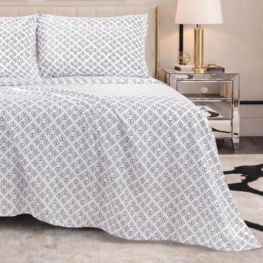 A neatly made bed features the Microfiber Sheet Set With Extra Pillowcases in a white and gray pattern, complemented by two pillows, a mirrored nightstand holding a lamp and decorative items, with part of a black and white rug visible on the floor.