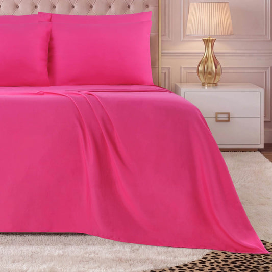 A neatly made bed with a bright pink Microfiber Sheet Set With Extra Pillowcases, next to a white nightstand with a gold lamp, on a light-colored shaggy rug in a softly lit room.