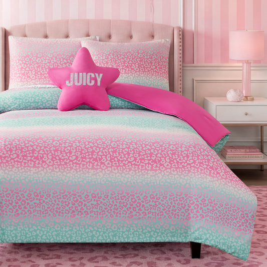 A vibrant kids’ bedroom highlights the Kids Rainbow Ombre Leopard Reversible Comforter Set, which features playful pink and mint leopard-print bedding. The room is accented with a pink star-shaped JUICY pillow, striped pink wallpaper, a coordinating pink lamp, and a subtle animal print pattern rug—perfectly capturing the fun and stylish Juicy Couture aesthetic.