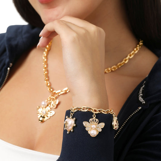 A woman in a dark jacket wears a gold chain necklace with a butterfly pendant and the Pearl & Icon Charm Bracelet, an adjustable gold-tone piece featuring pearls and butterfly charms, as she holds her hand near her chin.