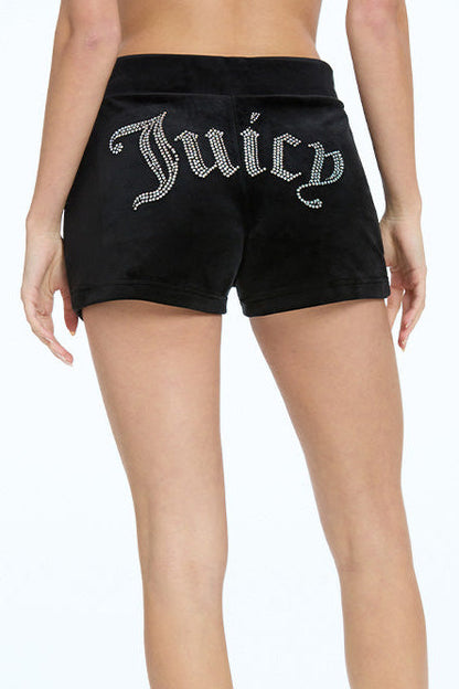 A person wears Big Bling Velour Track Shorts in black, featuring side pockets and “Juicy” in rhinestones across the back. The photo shows a rear view from waist to mid-thigh.