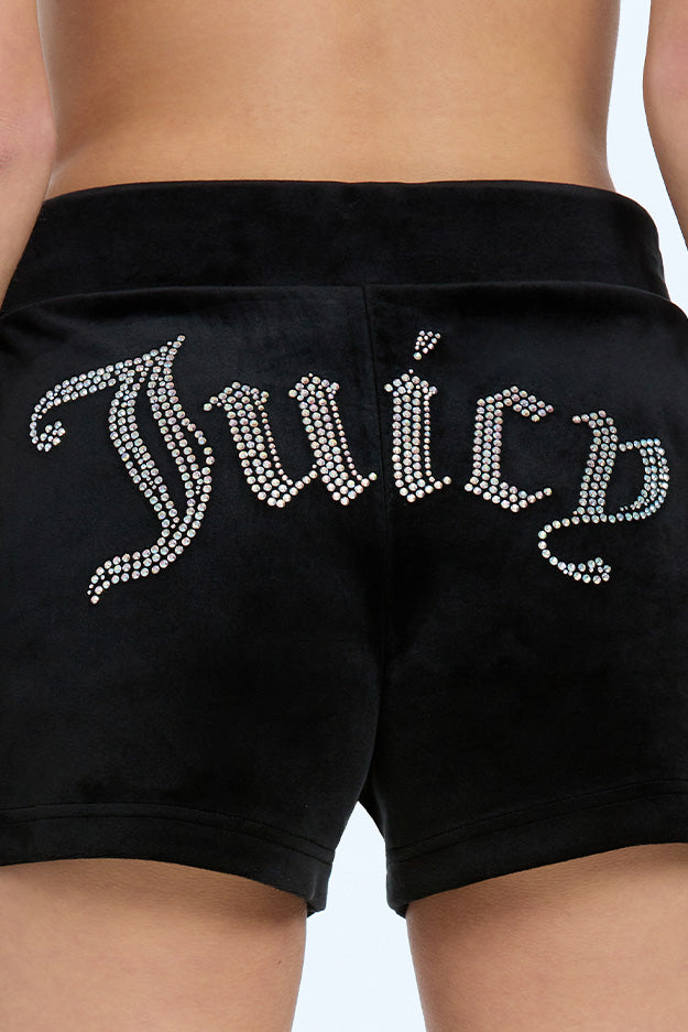 Wearing Big Bling Velour Track Shorts, this person adjusts the drawstrings for a perfect fit, showcasing the sparkling rhinestone lettering across the back.