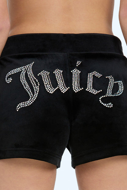 Wearing Big Bling Velour Track Shorts, this person adjusts the drawstrings for a perfect fit, showcasing the sparkling rhinestone lettering across the back.