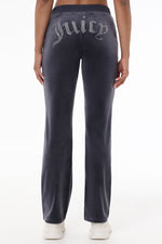 Someone wearing the OG Big Bling Velour Track Pants in dark gray with sparkling Juicy embellishment on the back, paired with white sneakers, shown from behind and waist down.