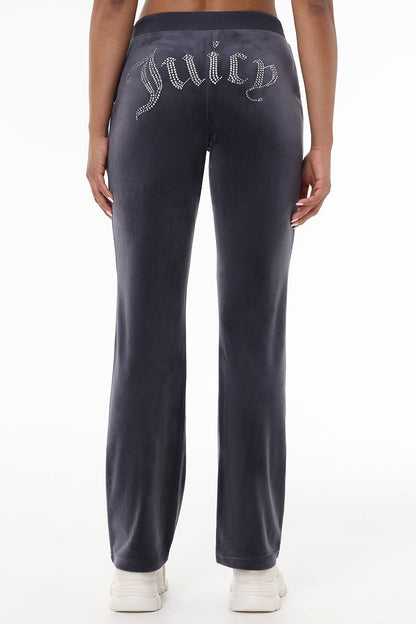 Someone wearing the OG Big Bling Velour Track Pants in dark gray with sparkling Juicy embellishment on the back, paired with white sneakers, shown from behind and waist down.