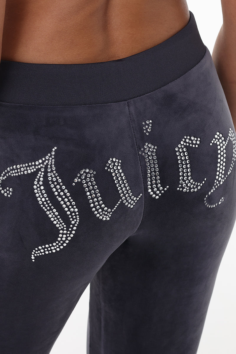 A close-up shows the back of a person wearing OG Big Bling Velour Track Pants, featuring a sparkling Y2K rhinestone Juicy embellishment across the backside.