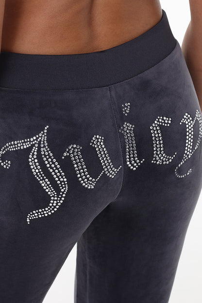 A close-up shows the back of a person wearing OG Big Bling Velour Track Pants, featuring a sparkling Y2K rhinestone Juicy embellishment across the backside.