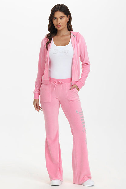A woman faces forward against a plain white background, wearing French Terry Embroidered Shorts in light pink with an embroidered logo, paired with a matching jacket and a white tank top. One hand is in her pocket.