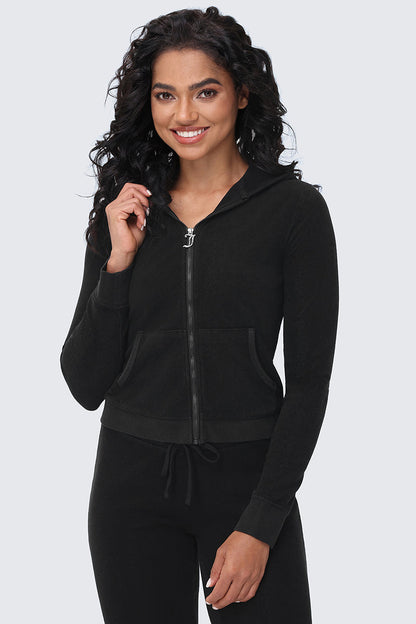 A woman with long curly hair wears the Big Bling Washed Terry Hoodie with front pockets and matching black pants, smiling while standing against a light gray background.