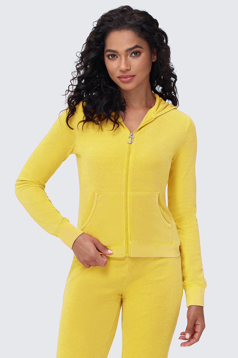 A woman with long, curly dark hair wears the Big Bling Washed Terry Hoodie in bright yellow with matching pants, standing against a light gray background and looking at the camera with a slight smile.