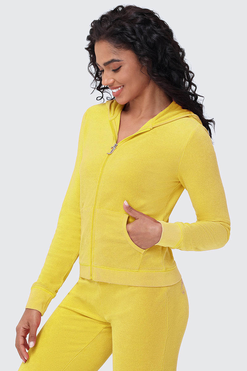 A woman with long curly hair smiles and looks down while wearing the Big Bling Washed Terry Hoodie in bright yellow, paired with matching pants, against a plain light gray background.