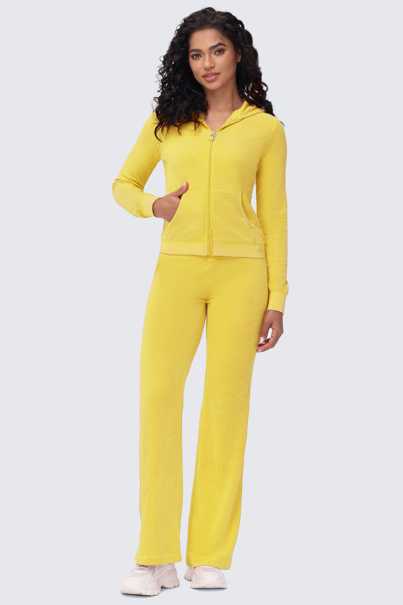 A woman with curly hair faces forward, wearing the Big Bling Washed Terry Hoodie and matching pants in bright yellow, paired with white sneakers against a light gray background.