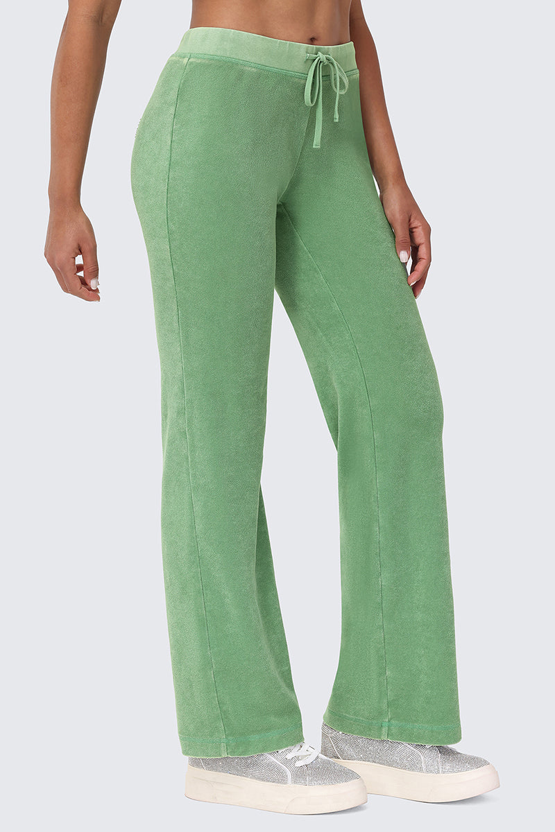 A person wears the Big Bling Washed Terry Track Pants in light green, featuring a wide-leg fit and drawstring waist, paired with white sneakers. The side view image is cropped from mid-torso down against a light gray background.