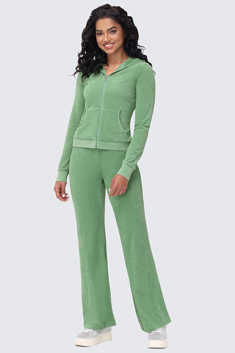 A woman with long curly hair wears Big Bling Washed Terry Track Pants and a matching rhinestone zip-up hoodie in light green, paired with white sneakers, smiling as she stands against a light gray background.