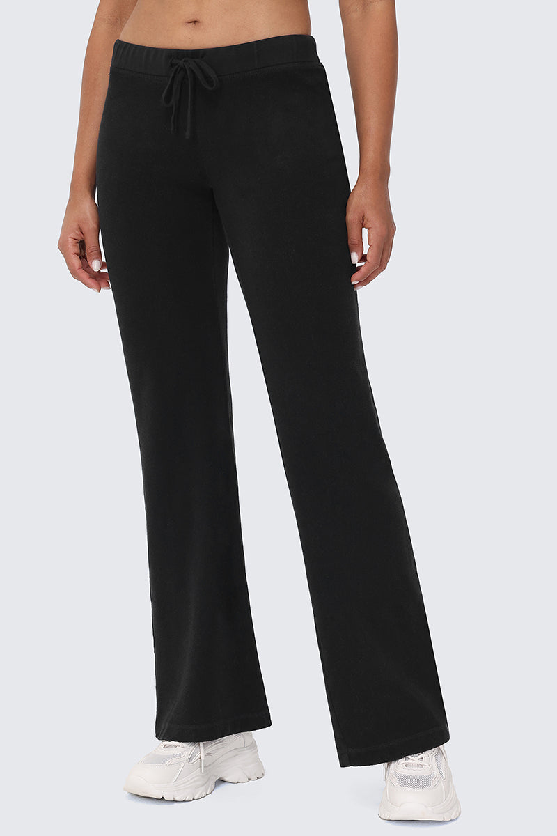 A person models the Big Bling Washed Terry Track Pants in black, featuring a drawstring waist and flared legs, paired with white sneakers against a plain light gray background. The person's face is not visible.