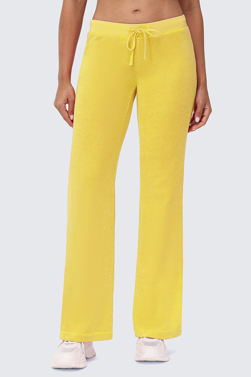 Wearing Big Bling Washed Terry Track Pants in bright yellow and white sneakers, a person stands against a plain light gray background with only their lower torso and legs visible.