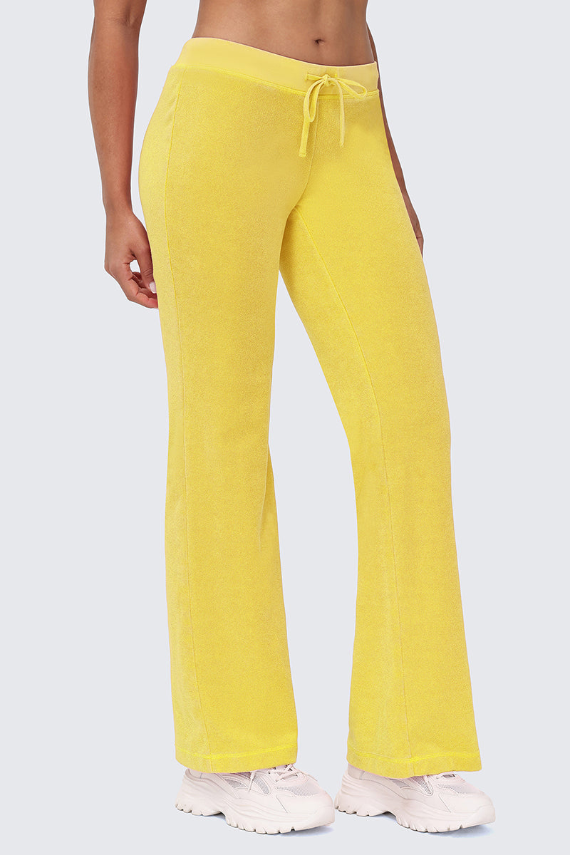 Wearing Big Bling Washed Terry Track Pants in bright yellow with a drawstring, paired with white sneakers. The cropped image, from shoulders down, features the person standing against a plain light gray background.