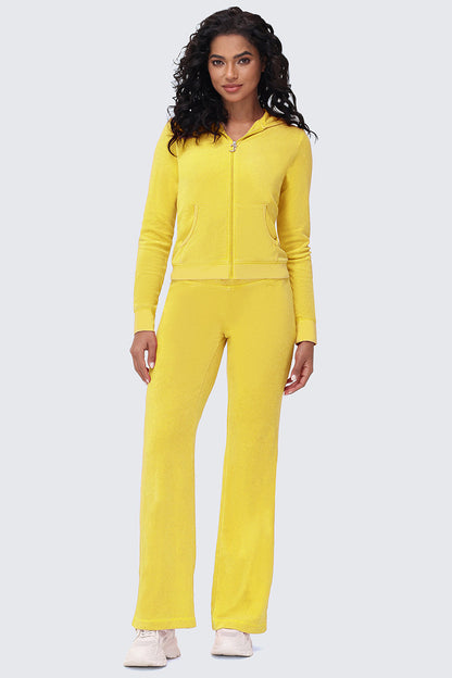 A woman with curly hair wears Big Bling Washed Terry Track Pants, a bright yellow zip-up hoodie, and light sneakers, standing against a plain light gray background.