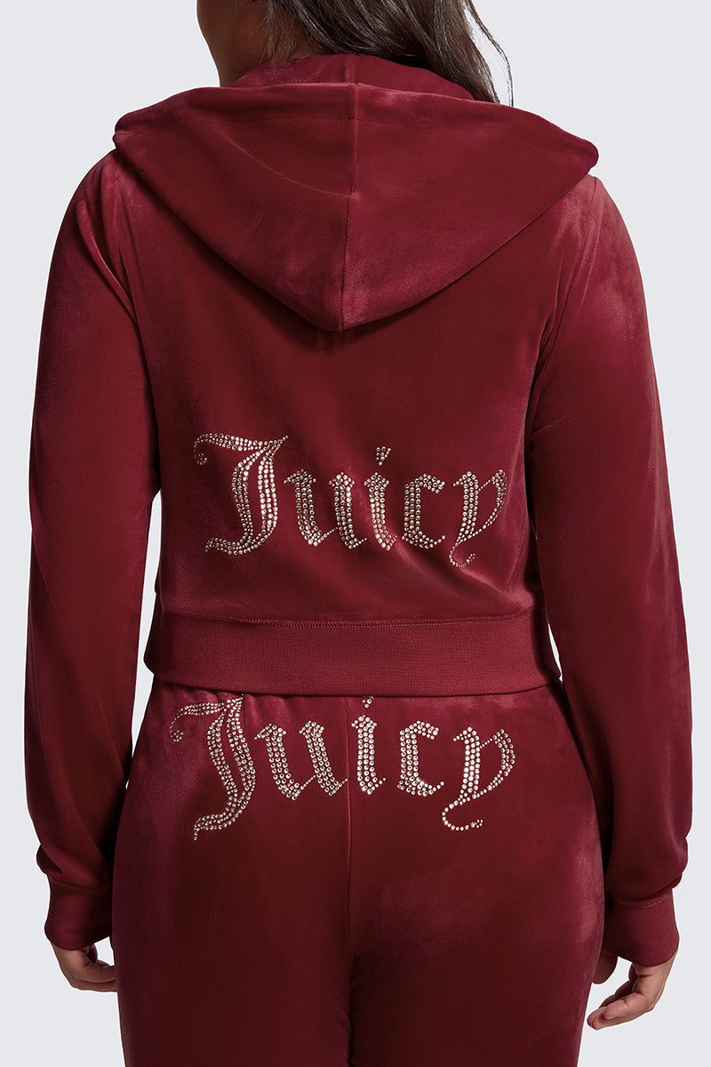 A woman wears the Plus-Size OG Big Bling Velour Hoodie, a maroon Y2K-inspired tracksuit featuring a hood, sparkling rhinestone "Juicy" on the back, and trendy thumbholes on the sleeves.