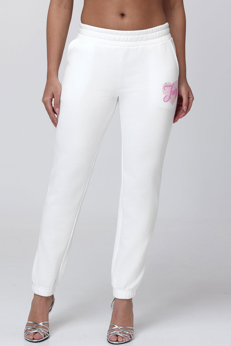 A person wears Sweetheart Fleece Sweatpants featuring a relaxed fit and pink embroidery on the left hip, paired with silver strappy high-heeled sandals. The image is cropped from mid-torso to feet.
