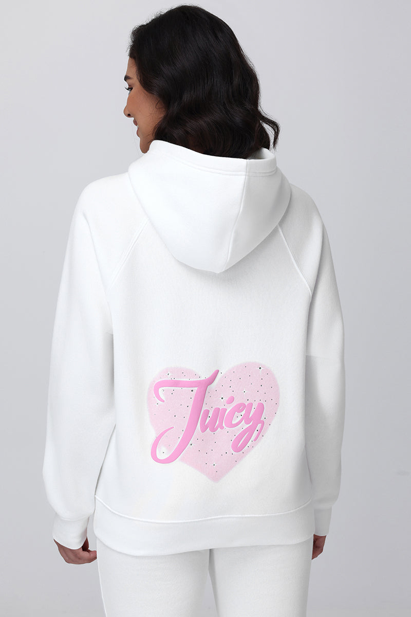 A woman models the Sweetheart Fleece Oversized Hoodie—white, oversized, with a large pink heart and “Juicy” script on the back—paired with white pants against a plain light background for a fresh, casual look.