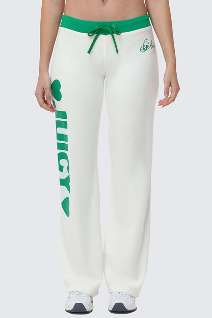 A person wearing Contrast Low Rise Track Pants featuring green trim, a green drawstring, "JUICY" and two green hearts printed vertically on the left leg, paired with white athletic shoes.