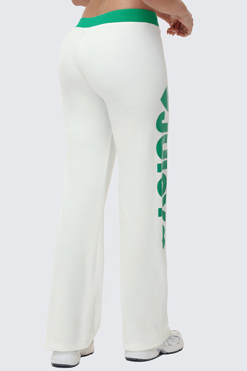 A person is seen from the back in sporty loungewear: white Contrast Low Rise Track Pants with a green waistband and bold green "JUICY" text on the left leg, paired with white sneakers, against a plain background.