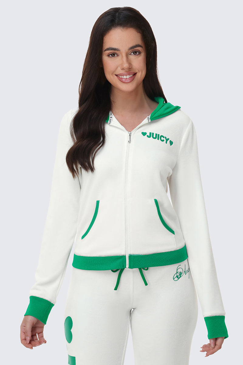 A woman with long brown hair smiles in front of a plain light gray background wearing the Contrast Trim Logo Hoodie—with green trim and JUICY text on the chest—and matching white sweatpants featuring green accents.