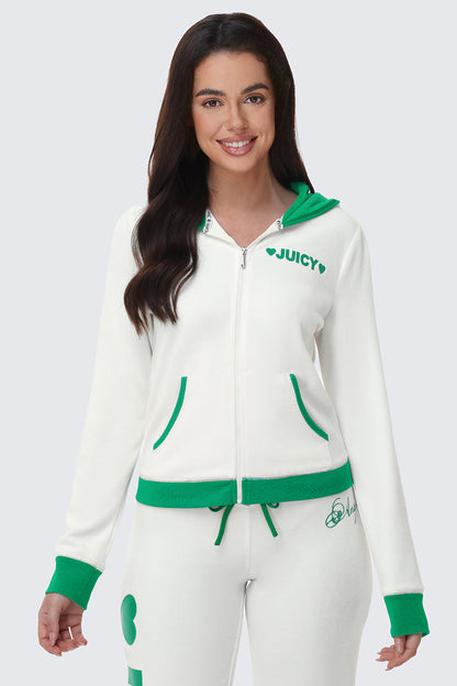A woman with long brown hair smiles in front of a plain light gray background wearing the Contrast Trim Logo Hoodie—with green trim and JUICY text on the chest—and matching white sweatpants featuring green accents.