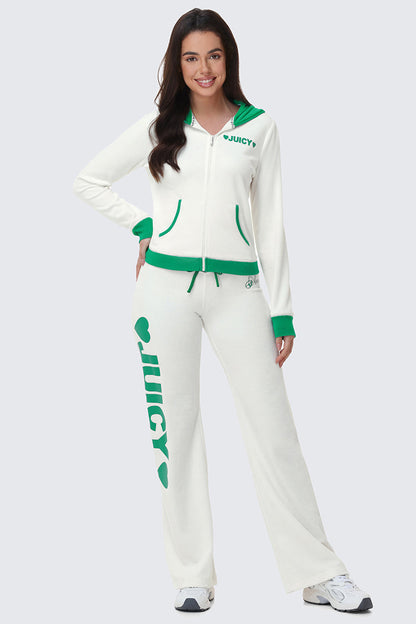 A woman with long brown hair smiles, wearing the Contrast Trim Logo Hoodie in white with green trim and matching pants. “JUICY” is printed on the chest of the hoodie and down one pant leg. She poses with one hand on her hip.