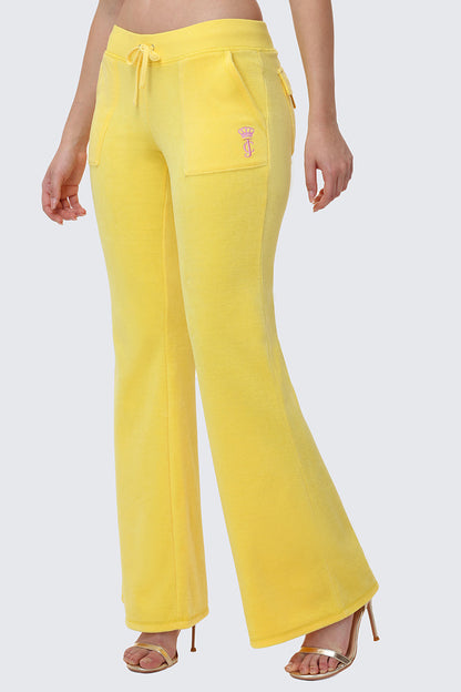 A person wears Heritage Cotton Velour Track Pants in juicy yellow with a drawstring waist, front patch pockets, and logo embroidery on the left pocket, styled with beige high-heeled sandals.