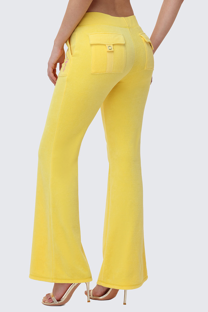 A person is shown from the back wearing bright yellow Heritage Cotton Velour Track Pants with a drawstring waist and large back pockets, paired with high heels, standing against a plain light gray background.