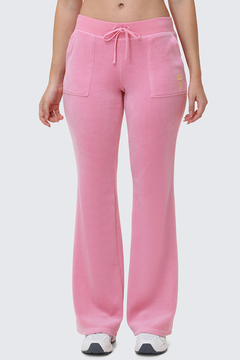 A person wearing Heritage Cotton Velour Track Pants in light pink, featuring front pockets and a drawstring waist, paired with white sneakers. Shown from the midriff down against a plain background.