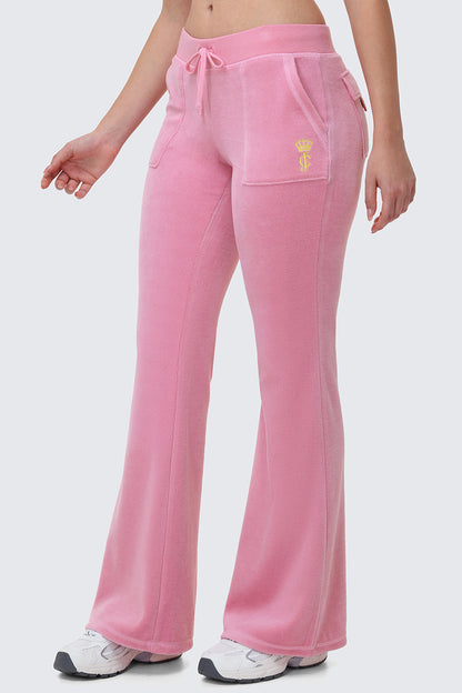 A person wearing Heritage Cotton Velour Track Pants in light pink with a drawstring waist, front pockets, and a small yellow crown logo, paired with white sneakers, shown from the waist down.