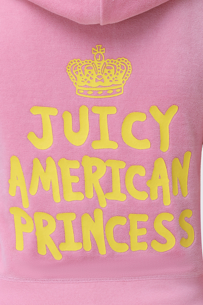 A close-up of the American Princess Heritage Hoodie in pink velour, showcasing a yellow crown logo above "Juicy American Princess" in bold, playful yellow letters.