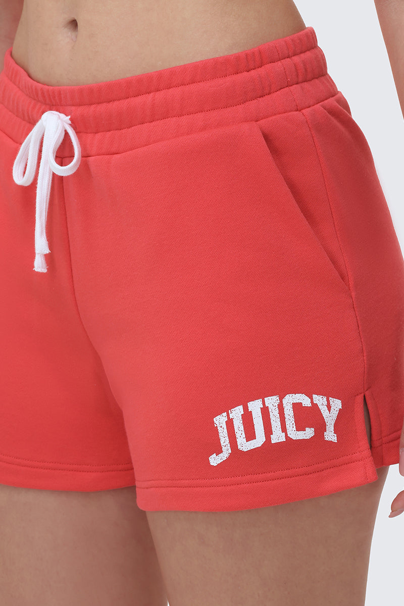 A close-up of a person wearing Collegiate Booty Shorts in bright red terry with a drawstring waist and the Juicy logo printed in white on the left leg.